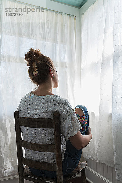 Frau vor einem Fenster mit Vorhängen sitzend