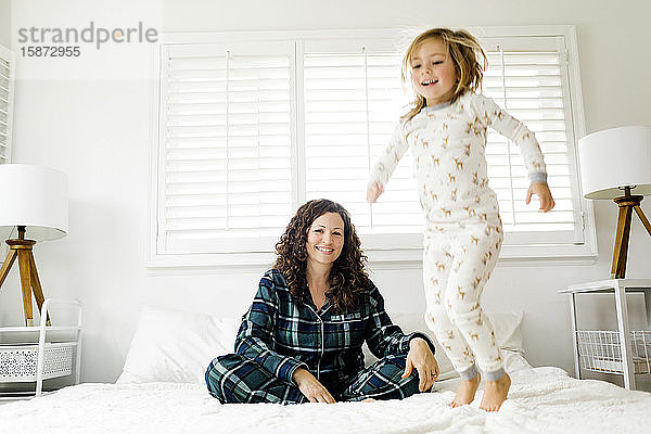 Auf dem Bett springendes Mädchen und ihre lächelnde Mutter
