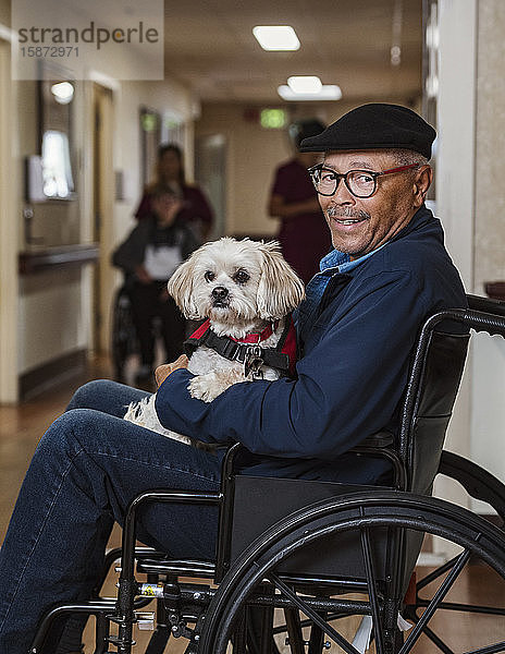 Lächelnder älterer Mann mit Hund im Rollstuhl