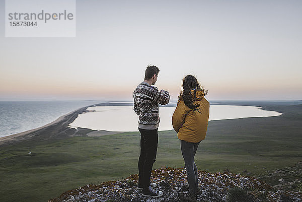 Junges Paar steht auf einem Hügel bei Sonnenuntergang