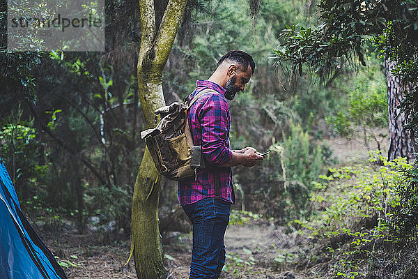 Mann mit Rucksack benutzt Smartphone im Wald