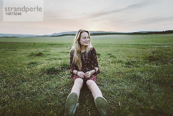 Lächelnde Frau im Kleid auf einem Feld sitzend