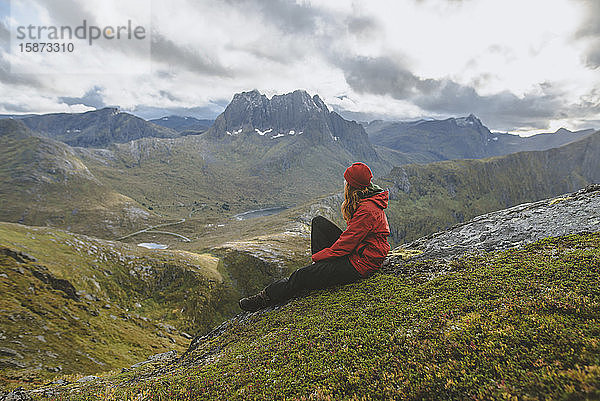 Junge Frau in roter Jacke auf einem Berg sitzend