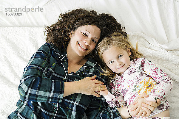 Hohe Winkelansicht von Mutter und Tochter im Pyjama auf dem Bett liegend