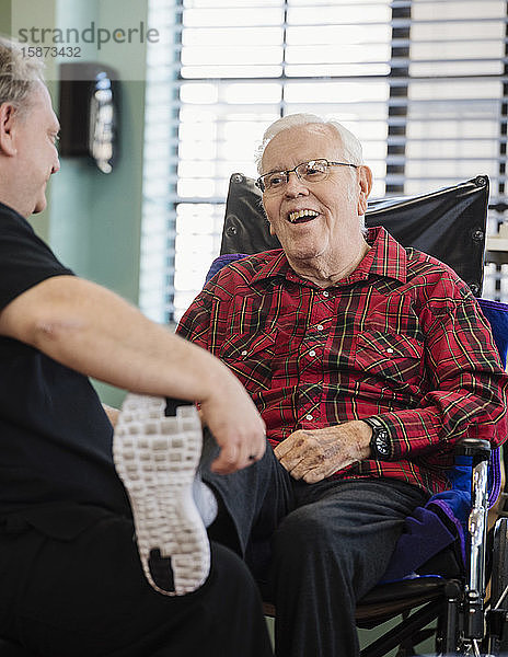 Krankenschwester hält lächelnd den Fuß eines älteren Mannes im Rollstuhl