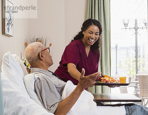 Lächelnde Krankenschwester hängt Essen an einen älteren Mann im Bett