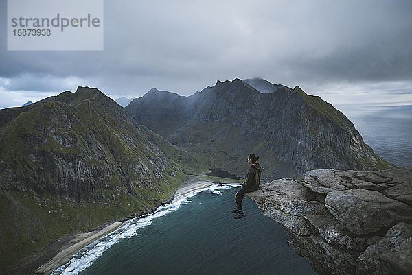 Mann sitzt auf einer Klippe am Berg Ryten auf den Lofoten  Norwegen