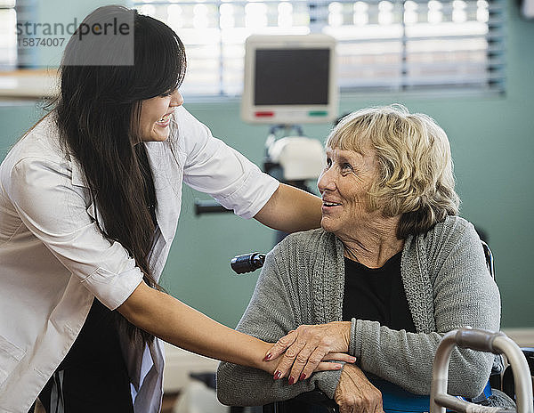Lächelnder Arzt und ältere Frau halten sich im Rehabilitationszentrum an den Händen