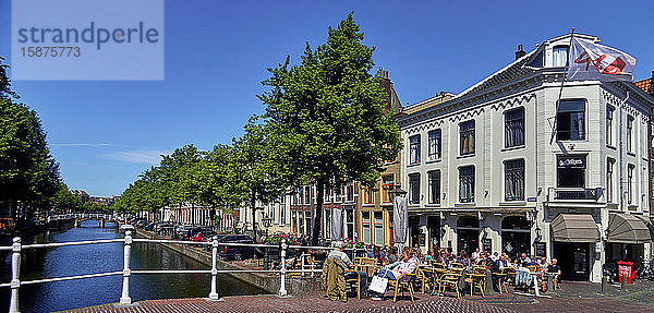 Stadt Leiden  Provinz Südholland  Niederlande  Europa  Menschen entspannen sich entlang der holländischen Gracht Rapenburg im historischen Zentrum von Leiden  Die Stadt Leiden ist bekannt für ihre weltliche Architektur  ihre Grachten  ihre Universität von 1590  die Geburtsstadt von Rembrand  die Stadt  in der im 16. Jahrhundert die erste Tulpe in Europa blühte