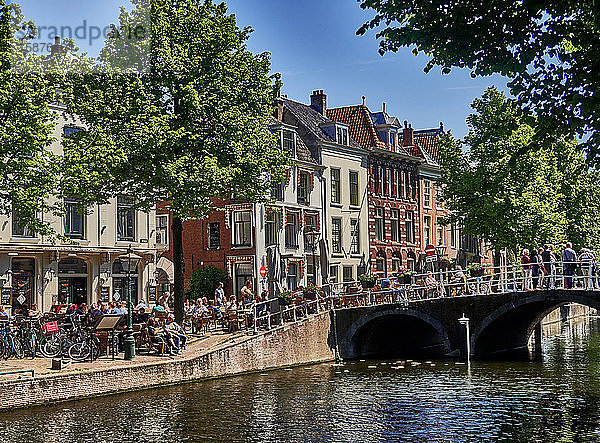 Stadt Leiden  Provinz Südholland  Niederlande  Europa  Menschen entspannen sich entlang der holländischen Gracht Rapenburg im historischen Zentrum von Leiden  Die Stadt Leiden ist bekannt für ihre weltliche Architektur  ihre Grachten  ihre Universität von 1590  die Geburtsstadt von Rembrand  die Stadt  in der im 16. Jahrhundert die erste Tulpe in Europa blühte