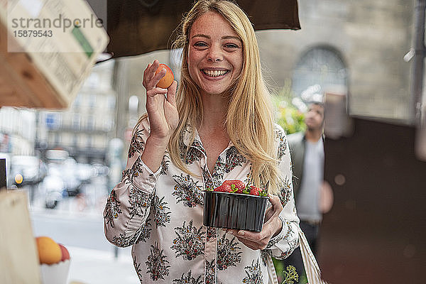 Junge Frau kauft Früchte an einem Marktstand