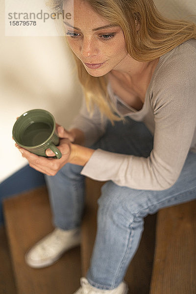 Junge Frau hält Tasse und sitzt auf einer Treppe