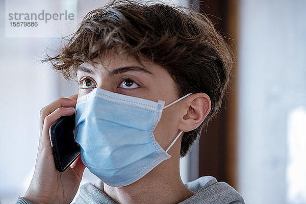 Nahaufnahme eines Teenagers mit medizinischer Maske  der während des Einschlusses mit seinem Smartphone spricht