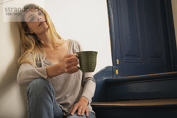 Junge Frau hält Tasse und sitzt auf einer Treppe