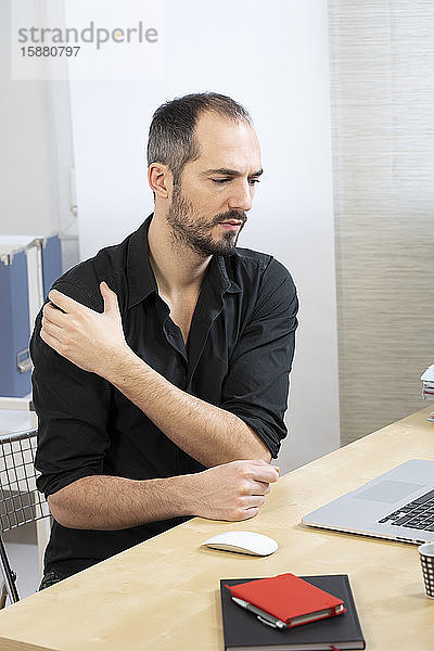 Ein Mann an seinem Schreibtisch mit Schulterschmerzen.