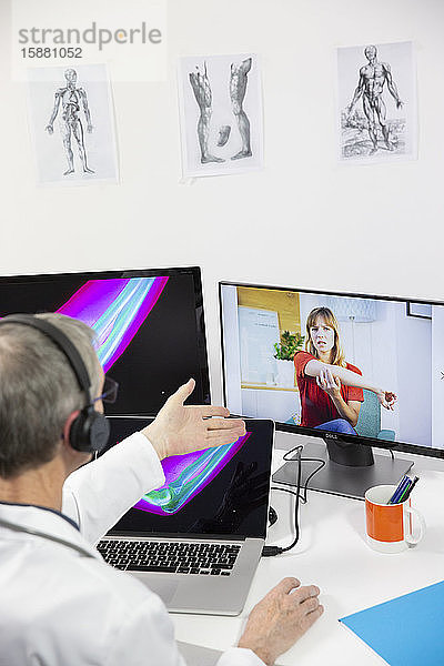 Eine junge Frau  die wegen Ellenbogenschmerzen und einer Röntgenaufnahme des Ellenbogens eine Videokonsultation mit einem männlichen Allgemeinmediziner durchführt.
