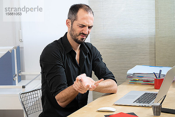 Ein Mann an seinem Schreibtisch mit Schmerzen in der Hand und im Handgelenk.