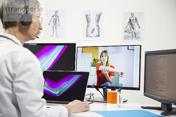 Eine junge Frau  die wegen Ellenbogenschmerzen und einer Röntgenaufnahme des Ellenbogens eine Videokonsultation mit einem männlichen Allgemeinmediziner durchführt.