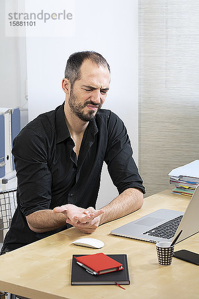 Ein Mann an seinem Schreibtisch mit Schmerzen in der Hand und im Handgelenk.