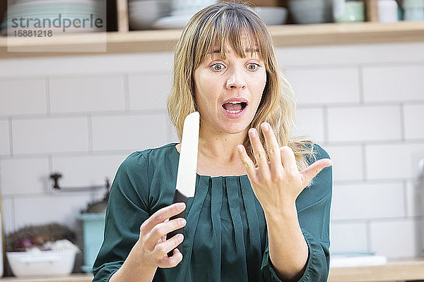 Eine junge Frau in ihrer Küche  die sich mit einem Küchenmesser geschnitten hat.