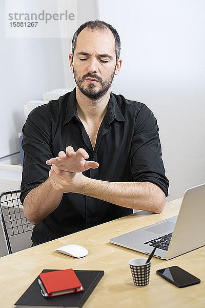Ein Mann an seinem Schreibtisch mit Handschmerzen.