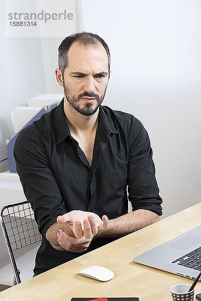 Ein Mann an seinem Schreibtisch mit Handschmerzen.
