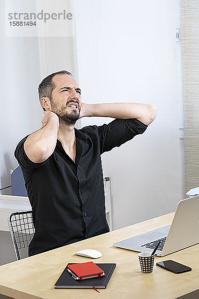 Ein Mann an seinem Schreibtisch mit Nackenschmerzen.