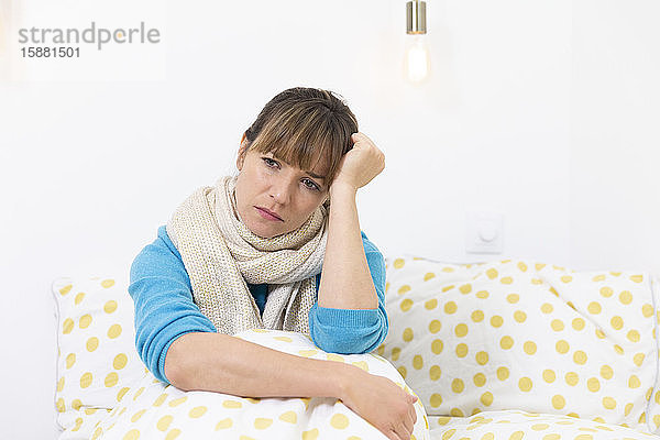 Eine junge Frau liegt im Bett und leidet an einer grippeähnlichen Erkrankung mit Migräne.