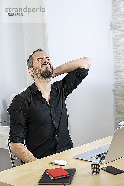 Ein Mann an seinem Schreibtisch mit Nackenschmerzen.