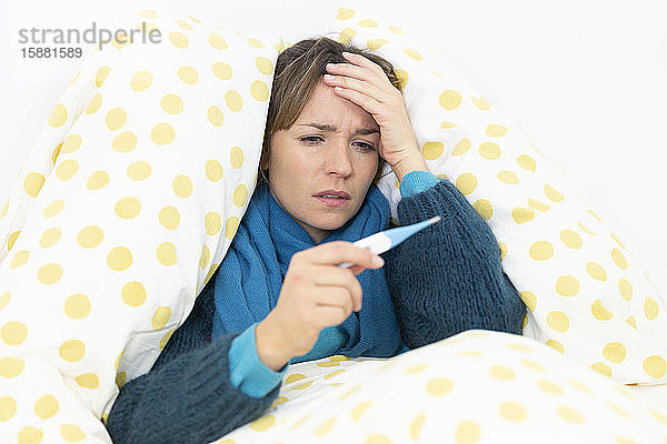 Eine junge Frau im Bett  die an einer Grippe erkrankt ist  mit einem Thermometer.