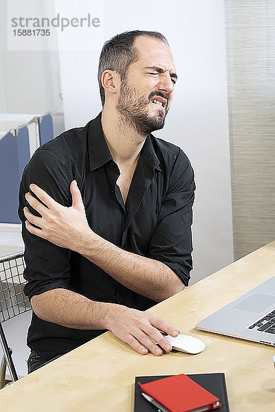 Ein Mann an seinem Schreibtisch mit Schulterschmerzen.