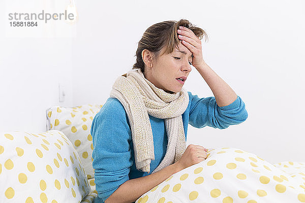 Eine junge Frau liegt im Bett und leidet an einer grippeähnlichen Erkrankung mit Migräne.