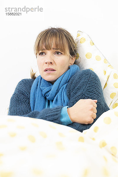 Eine junge Frau liegt im Bett und leidet an einer grippeähnlichen Erkrankung.