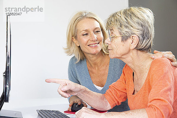 Eine Frau in den Fünfzigern hilft einer älteren Frau bei der Benutzung eines Computers.