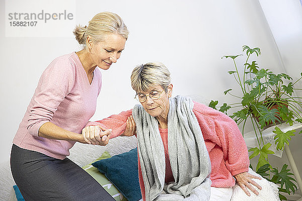 Eine Frau in den Fünfzigern hilft einer älteren Frau beim Aufstehen.