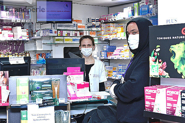 Apotheker und Kunden mit Schutzmasken und Handschuhen in einer Apotheke zur Zeit der Coronavirus-Pandemie  durch die COVID-19 verbreitet wird.