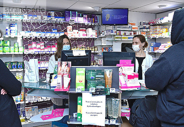 Apotheker und Kunden mit Schutzmasken und Handschuhen in einer Apotheke zur Zeit der Coronavirus-Pandemie  durch die COVID-19 verbreitet wird.
