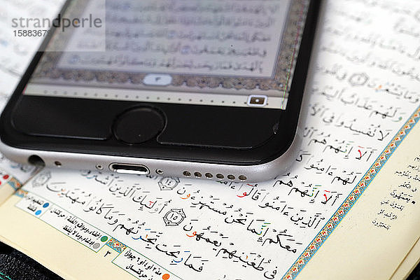 Digitaler Koran auf einem Smartphone und heiliges Koranbuch. Nahaufnahme.