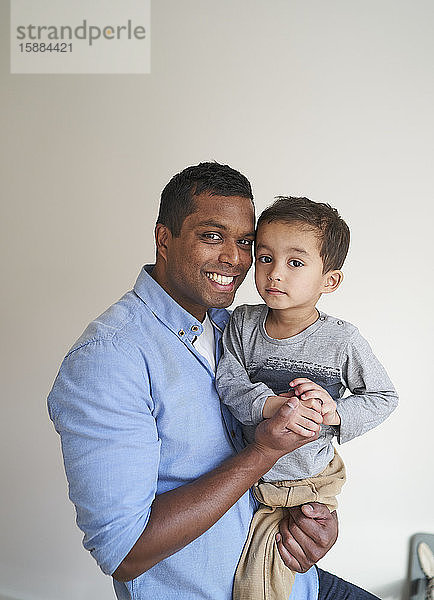 Ein Mann hält seinen Sohn und lächelt  während beide in die Kamera schauen.
