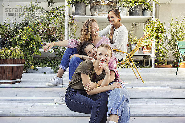 Vier lächelnde Frauen sitzen in einem Innenhof mit Pflanzen im Hintergrund.