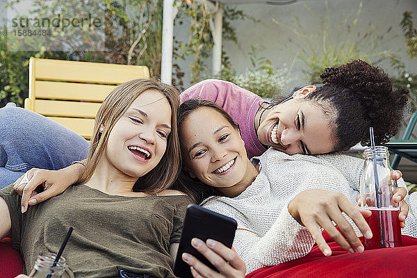 Drei Frauen  die zusammen faulenzen  lachen und auf ein Mobiltelefon schauen.
