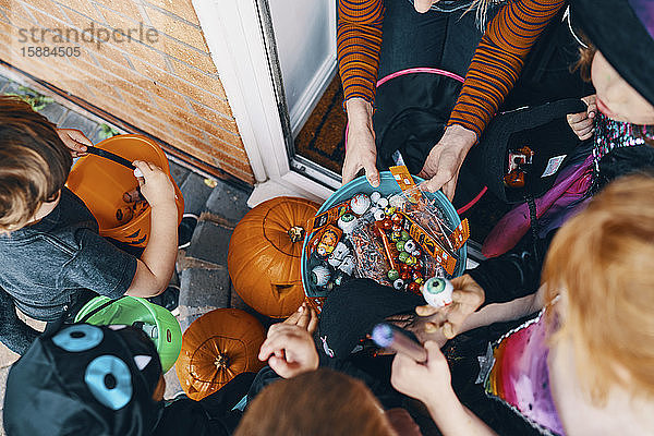 Draufsicht auf eine Gruppe von Kindern an einer Haustür  die an Halloween Süßigkeiten aus einer Schüssel nehmen.