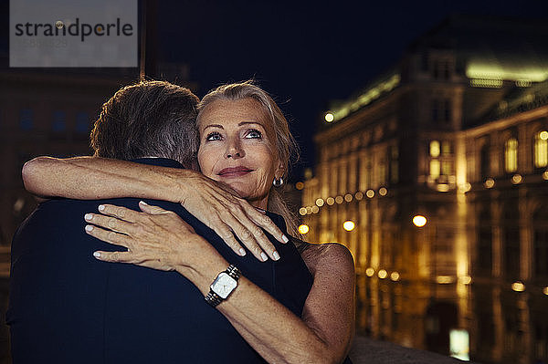 Eine Frau umarmt ihren Partner und lächelt ihm bei einem Abend in Wien über die Schulter.