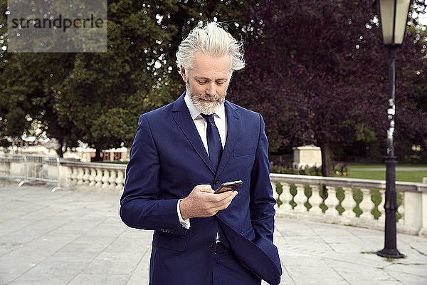Ein Mann in Anzug und Krawatte steht in einem Gang und schaut auf ein Mobiltelefon.
