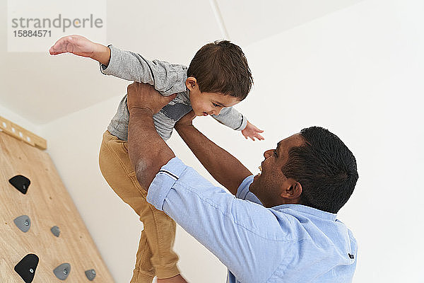 Ein Vater hält seinen Sohn über dem Kopf  beide lächeln  der Sohn mit weit ausgestreckten Armen.