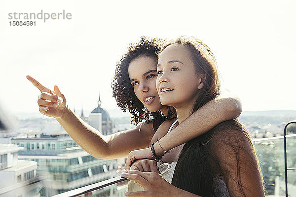 Zwei Frauen auf einem Balkon mit Blick auf Wien  eine mit einem Arm auf den Schultern der anderen und zeigend.