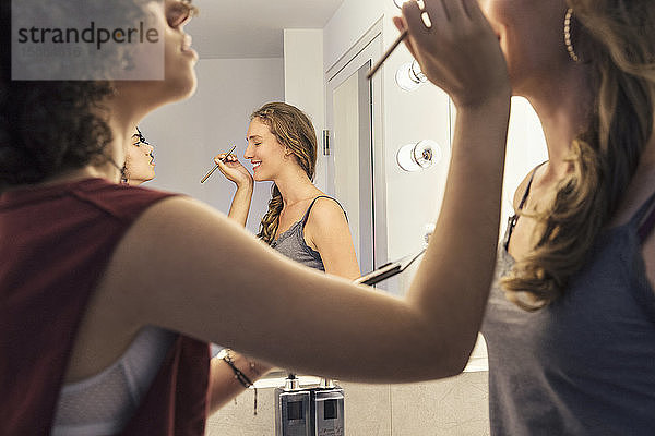 Eine Frau schminkt eine andere Frau mit einer Spiegelung im Spiegel.