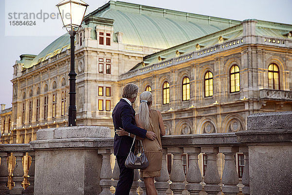 Rückansicht eines Paares  das über eine Balustrade an einer Wiener Straße blickt.