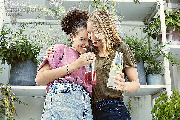 Zwei Frauen  die eng beieinander stehen und auf einer Terrasse ein Getränk trinken
