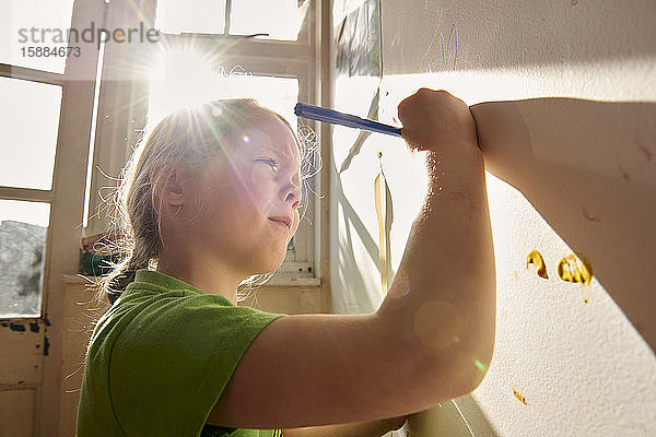 Lächelndes Mädchen im Haus während der Corona-Virus-Krise  Malerei an einer Wand.